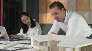 Ev planı çizmek için birlikte çalışan yetenekli mimar mühendisi. Mimar takımı, mimari model, plan ve dizüstü bilgisayarla ofis masasına yerleştirilen ev inşaatı hakkında tartışır. Yönlendirici.