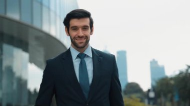 Profesyonel iş adamı hareket ediyor ve kameraya bakarken ayakta duruyor. Gülümseyen yönetici kameraya kendinden emin bir şekilde gülümsüyor. Mimari binada takım elbiseli yatırımcıların yakın çekimi. Sevinçli..