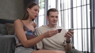 Genç çift, kredi kartıyla ödemek için internet üzerinden ödeme uygulaması ve dijital cüzdan kullanarak yatak odasında oturuyor. Mobil internet üzerinden alışveriş ve modern alımlar. Düzenle