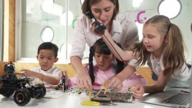 Genç, beyaz bir öğretmen çeşitli öğrencilere elektronik yönetim kurulunu öğretiyor. Çok kültürlü çocuklar dijital elektrikli aletleri ve ana kartı çip ve kablolar kullanarak tamir etmeyi öğrenirler. Etkinlik.
