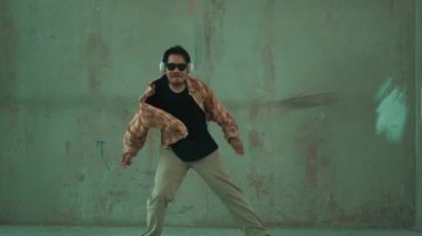 Çimento arka planında kulaklıktan müzik dinlerken sıradan sokak dansı yapan çekici İspanyol dansçı. Break dans gösterisinin hareketli çekimi. Açık hava sporu 2024 hiphop..