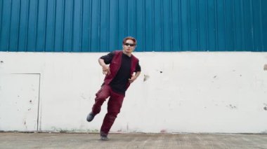 Beyaz arka planda break dans pratiği yapan yakışıklı bir sokak dansçısı. Hip hop tarzı giyinen sporcu, mavi arka planlı bir sokakta müzik eşliğinde ayak sesleri çıkarıyor. Açık hava sporu 2024 hiphop..