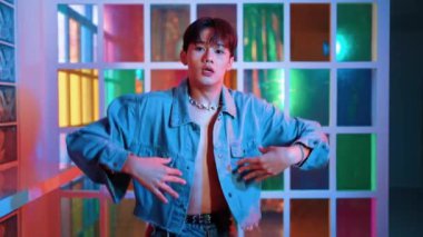 Kameraya bakarken kollarını esneten seksi kıyafetli Asyalı dansçı. Profesyonel sanatçı gece kulübünde renkli neon ışıkları canlı bir şekilde dururken serbest stil dansı yapıyor. Mutluluk.