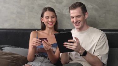 Genç çift, kredi kartıyla ödeme yapabilmek için internet üzerinden ödeme uygulaması ve dijital cüzdan kullanarak yatak odasında oturuyor. Mobil internet üzerinden alışveriş ve modern alımlar. Düzenle