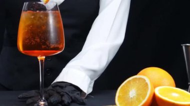 Makrografi, bir barmenin yetenekli ellerine tanık olun. Aperol Spritz kokteylinde dikkat çekici bir siyah arka plana karşı ustalıkla buz karıştırıyorlar. Her yakın plan el yapımı kokteyl. Geliştirilebilir.