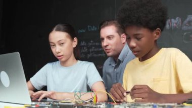 Kafkas öğretmeni mühendislik kodlarını öğretirken dizüstü bilgisayarı gösteriyor. Lise öğrencisi mutlu bir şekilde öğrenirken ve programlama öğrenirken bilgisayar kullanarak çalışan eğitmen. Öğretim