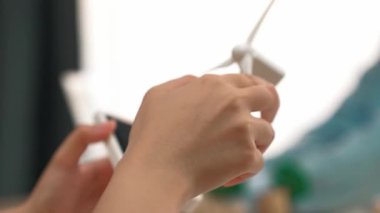 İş kadını temiz enerjiyle temsil edilen yel değirmeni modelini tutuyor. Tahta blok sembolize ekoloji evi ve yeşil güç grafiği masanın üzerinde dağılıyor, iş adamı dizüstü bilgisayarla çalışıyor. Tanımlama.