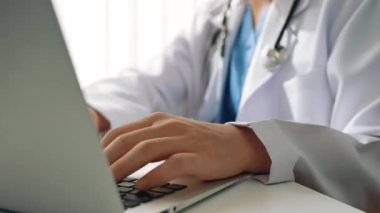 Hastanedeki doktor masasında oturup dizüstü bilgisayar üzerinde çalışıyor. Hasta test sonuçlarını teşhis ediyor, hastalıklar ve hastalıklar için tedavi planı geliştiriyor. Sağlık personeli ve sağlık hizmetleri. Ağır çekim. Katı.