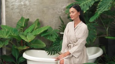 Modern otelde küveti olan tropikal ve egzotik bir spa bahçesi ya da yemyeşil yeşillik arka planıyla çevrili rahat ve sağlıklı yaşam tarzının tadını çıkaran bornozlu bir kadınla tatil köyü. Blithe