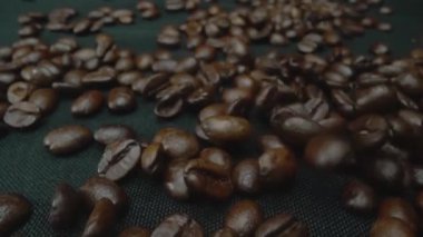 Karışık aromalı kahve çekirdeği yığını masaya saçılmış ve kavrulmuş kahve çekirdekleri etrafa saçılmış siyah arkaplanla çevrilmiş. Makrografi. Ağır çekim. Pabulum.