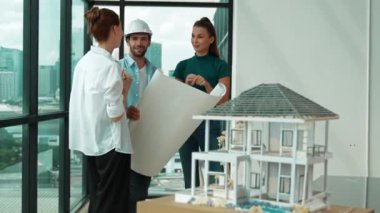 Profesyonel mimar mühendis ekibi konuşuyor, paylaşıyor, tasarım hakkında beyin fırtınası yapıyor. Yönetici planı dinlerken genç mimar plan yapıyor. İzleme