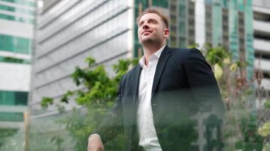 Kafkasyalı iş adamı cep telefonunu tutuyor ve gökdelen manzarasına bakıyor. Modern binanın çatısında duran yetenekli erkek lider. Kafkasyalı yönetici gözlerini dinlendirirken telefona bakar. Urbane.