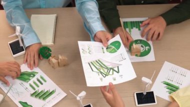 Eko evi projesini yel değirmeni tasarım modeli ve karbon ayak izini azaltmak için yeşil enerji kullanım grafiği ile toplantı masasında tartışan harika bir iş ekibi. Dünyayı kurtarın. Eline odaklan. Tanımlama.