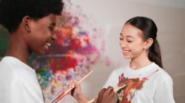 Resim dersinde, renkli duvarda, boyalı beyaz gömlekleri boyayarak gülümseyen farklı çocuklar. Tecrübe alışverişini temsil etmek, birbirimizi öğrenmek. Öğretim