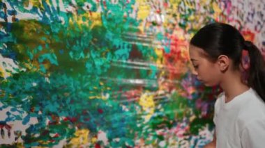 Genç mutlu kız renk tepsisini tutuyor ve fikri ifade etmek ve el iziyle hayal gücünü geliştirmek için renkli duvarları boyuyor. Resim dersinde odayı dekore etmek için beyaz kız pulu. Öğretim