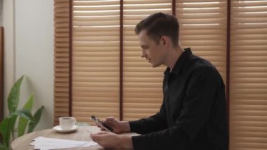 Masada oturan mutlu adam, faturaları kredi kartıyla öderken gülümsüyor, tüm faturaları tek seferde ödemenin kolaylığını takdir ediyor ve kredi kartının sunduğu ödülün tadını çıkarıyor. Düzenle