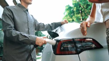 Yavaş çekim çift yazın yeşil sürdürülebilir şehir açık bahçesinde elektrikli araba şarj ile seyahat elektrikli aracın temiz yeniden şarj edilebilir enerjisi için kentsel sürdürülebilirlik yaşam tarzı olarak