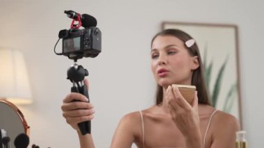 Sosyal medya için güzellik ve kozmetik video içeriği hazırlayan genç bir kadın. Güzellik blogcusu kameraya gülümserken seyircilere ve takipçilere güzellik bakımını gösteriyor. Düzenle