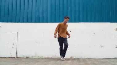 İspanyol adam kollarını açıp duvarın önünde dans ediyor. Dansçı ya da koreografın günlük kıyafetleriyle hip hop tarzında break dans yaparken ki görüntüsü. Açık hava sporu 2024 hiphop..