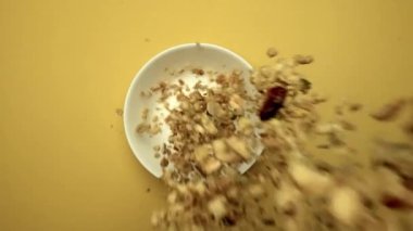Sağlıklı mısır gevreğinin sarı arka planda süt dolu beyaz kaseye düşüşünün en alttaki görüntüsü. Mısır gevreğini yaklaştır ve dondurulmuş kuru çilekle birlikte kaseye bırak. Ağır çekim. Kahvaltıda. Geliştirilebilir.