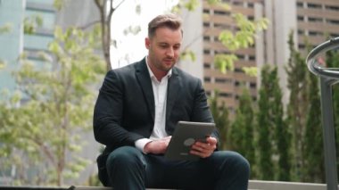 Green City 'de otururken tablet üzerinde çalışan iş adamlarına yakın durun. Düşük açılı kamera, yönetici tabletini kullanarak uzaktan çalışırken finansal veri analizini tarıyor. Urbane.