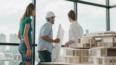 Gökdelene bakıp bir proje planı okurken, günlük kıyafetli akıllı mimar mühendis ekibi konuşuyor. Profesyonel yönetici takımı ev inşaatı hakkında beyin fırtınası yapıyor. Arkadan bak. İzleme