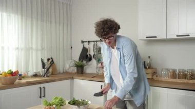 Mutlu baba yemek pişirirken müziğe geçiyor ve modern mutfakta öğle yemeği hazırlıyor. Aktif baba, sebze ve mutfak gereçleri ile çevrili sağlıklı yemek ya da salata yaparken şarkıyla dans ediyor. Pedagoji.
