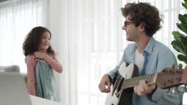Çekici beyaz bir baba gitar çalarken tatlı bir kız müzik eşliğinde dans ediyor. Mutlu baba ve Amerikalı kız birlikte vakit geçirirken akıllı çocuk müzik yapıyor. Aile eğlence konsepti. Pedagoji.