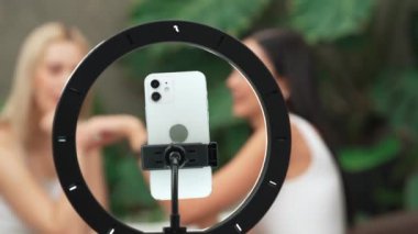 Telefon kamerasıyla odaklan iki güzel kadın içeriği yaratıcısı ya da arka planda güzellik blogcusu doğal bahçede kozmetik ve güzellik bakımı videosu çekiyor. Blithe