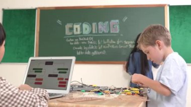 Kafkas arkadaşı STEM sınıfında elektrik panosunu tamir ederken Asyalı çocuk kodlama programı. Enerjik öğrenci kodlama mühendisliği komut yazarken ve yapay zeka yazılımını programlarken tahtada duruyor. Pedagoji.
