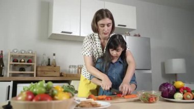Zeki beyaz anne ve Asyalı kız birlikte yemek pişiriyor ve sebze doğruyor ya da akşam yemeği için salata hazırlıyor. Mutlu anne ve kız taze yemekle sağlıklı yemek yapıyorlar. Sağlıklı gıda konsepti. Pedagoji.