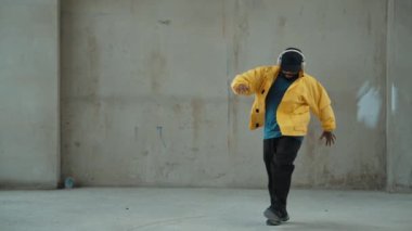 Hippi sokak, şehir merkezinde ayak izleri gösteriyor ya da pratik yapıyor. Break dansçının hareket halindeyken kulaklıktan müzik dinlediği sahne. Açık hava sporu 2024. Gri arka plan. Hip hop modası. hiphop.