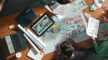 Planı elinde tutan inşaat mühendisi ekibinin en iyi görüntüsü ve dizüstü bilgisayar, proje planı ve planıyla masada duruyor. Yapışkan notları planlayan ve yazan yetenekli proje yöneticisinin havadan görünüşü. Sempozyum.