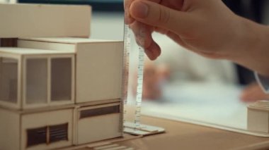 Cetvel ölçü evi modelini kullanan yetenekli profesyonel mühendis elini kapatırken, genç yetenekli mimar da taslak çiziyor. Yaratıcı ve profesyonel tasarım. Eline odaklan. Tertemiz..