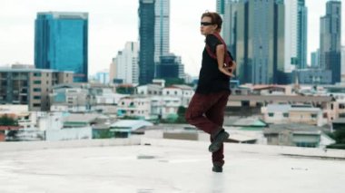 B-boy dans gösterisi profesyonel sokak dansçısı çatıda gökyüzü dövüşçüsüyle, şehir manzaralı. Çekici Asyalı hipster enerjik adımlar atıyor. Aktif break dans. Açık hava sporu 2024 hiphop..