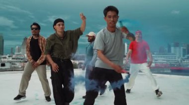 Bir grup çok kültürlü hippi çatıda işaret fişeği çalıyor. Zenci dumanı tutan çekici bir sokak dansçısı hip-hop müzik eşliğinde break dans yapıyor. Açık hava sporu 2024. Sokak dansı. hiphop.