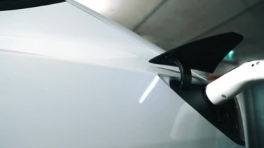 Yavaş çekim yakın EV elektrikli araba şarj istasyonunda fişe takılı, şehir merkezindeki alışveriş merkezinin otoparkında şarj bataryasını şarj ediyor. Elektrikli araç iç organları için temiz yeşil sürdürülebilir enerjisi var.
