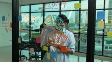 Akıllı proje yöneticisi cam duvara yapışkan notlar ve planlama stratejisi için zihin haritası yazarken, aynı zamanda çok kültürlü iş adamları da şehir manzaralı iş planlarını tartışıyorlar. İzleme