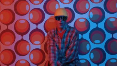 Profesyonel break dansçı, parti sahnesinde balon arka planlı gözlük takıyor. Havalı giyinen yetenekli bir sanatçı enerjik hareketler ve ayak sesleri göstererek müziğe yöneliyor. Mutluluk.