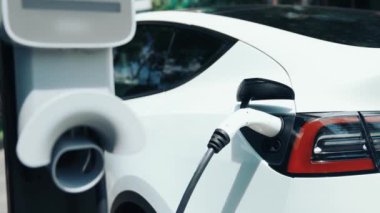 Yavaş çekim EV elektrikli araba yazın yeşil sürdürülebilir şehir parkı bahçesinde şarj oluyor. Elektrikli araç iç organları için kentsel yaşam tarzında sürdürülebilir temiz şarj edilebilir enerji