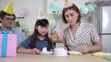 Kafkasyalı anne doğum günü pastasını kesiyor ve babaya verirken tatlıyı ayırıyor. Mutlu aile, kızının doğum gününde masada otururken parti şapkası takar. Özel durum konsepti. Pedagoji.