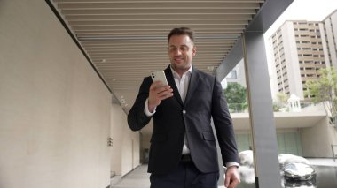 Happy proje yöneticisi koridorda yürürken cep telefonunu kontrol ediyor. Profesyonel iş adamı başarılı projesini kutlarken ya da satışları artırırken takım elbise giyer ve bavulu toplantı için tutar. Urbane.