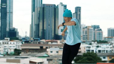 Beyaz tenli dansçı çocuk çatıda sokak dansı yapıyor şehir siteleriyle ya da şehirlerle. Genç adamın sokak dansı yaparken dondurucu poz vermesi. Açık hava sporu 2024. ÇalışmaComment.