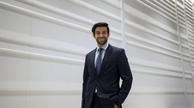 Gülümseyen iş adamı beyaz arka planda dururken kameraya bakıyor. İş elbisesi giyerken kameraya gülümseyen başarılı adamın yakın çekimi. Mutlu yönetici kameraya bak. Sevinçli..