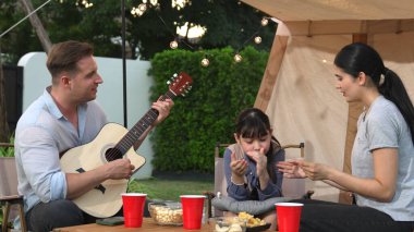 Aile birlikte kamp yapıyor. Anne ve kızı, babasının gitar çalışını dinliyor. Ebeveynler, genç nesil arasında iletişim kurmak ve zaman geçirmek için açık hava kamp faaliyetlerini kullanırlar. Uyumsuzluk.