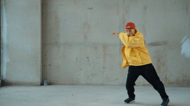 Beyaz hipster sokak, şehir merkezinde ayak sesleri gösteriyor ya da pratik yapıyor. Hareketli genç break dansçı hareketi ve kol ve bacak esneme hareketi. Açık hava sporu 2024. Gri arka plan. ÇalışmaComment.