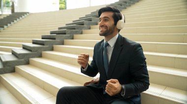 Proje yöneticisi merdivenlerde otururken kulaklıktan müzik dinliyor ve eğleniyor. Profesyonel iş adamı dans ederken ve müzik eşliğinde takım elbise giyer. Mutlu adam komik bir şarkı dinler. Sevinçli..