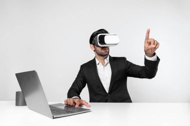 Bilgisayarla masada otururken ve VR gözlüğü takarken veri analizine bakan yetenekli bir iş adamı. Proje yöneticisi sanal gerçeklik sistemini kullanarak ya da metaevrende bağlantı kurarak çalışıyor. Sapma.