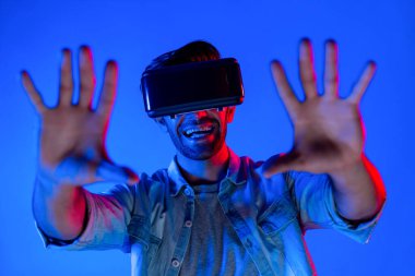 Heyecan verici bir sporcu el hareketi yaparken VR gözlüğü takıyor. Yetenekli genç ayakta duruyor ve teknolojik yenilikleri kullanarak gelecekteki sanal dünya programını veya metaevreni inceliyor. Sapma.