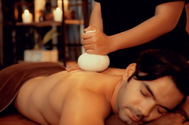 Sıcak bitkisel top spa masaj vücut tedavisi, masör erkek vücuduna nazikçe şifalı bitki torbası bastırıyor. Aromaterapi tesisinin sakinliği ve dinginliği kaplıca salonundaki mumların sıcacık ışığında. Sessiz.